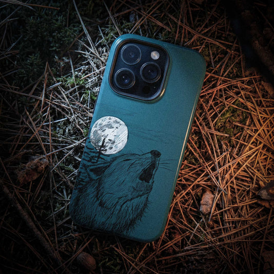 Rugged lifestyle shot of the Wild Wolf Howling phone case on a bed of pine needles in a New England forest setting.
