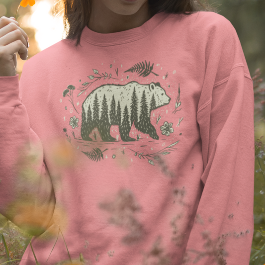 Wandering Bear Women's Sweatshirt worn by a model, showcasing a nature-inspired bear silhouette filled with trees, wildflowers, and ferns.